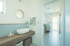 和室のバックヤードに設けたサニタリー。洗面室からランドリー、勝手口までが一直線につながり、家事の時短に貢献する間取りに。アールのラインがやさしさを添える丸い鏡、造作の洗面台、ブルーのタイルが絶妙に調和しています。