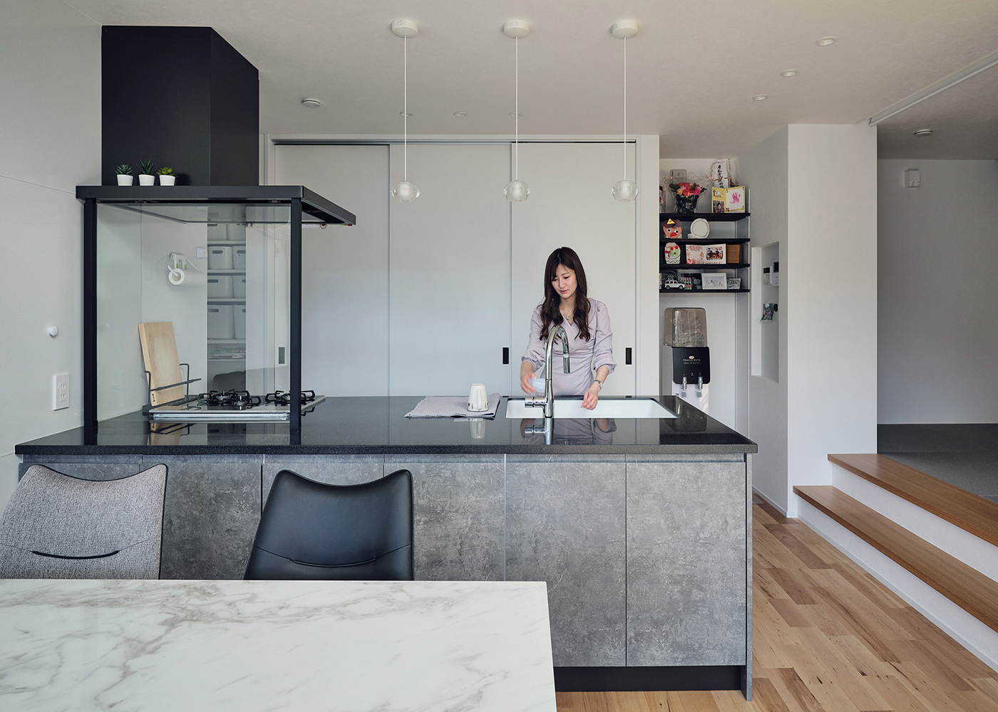 平屋建築ブルーハウス【デザイン住宅、間取り、ペット】奥さまこだわりのぺニンシュラ型キッチンは、奥行きが1mもあり、作業がしやすい。背面のハイドアを用いた「隠す収納」は大容量で、天井いっぱいまでものをしまえる。すぐ横には小上がりの畳コーナーを用意。子どもの様子を見守りながら炊事ができる