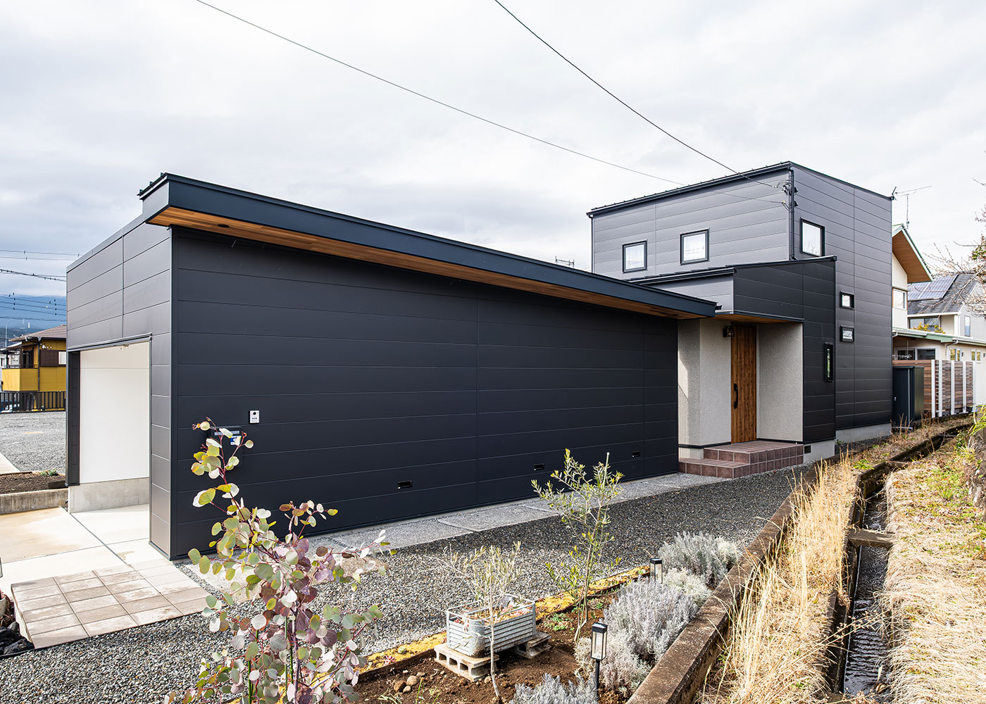 R＋house御殿場（岳南建設）【省エネ、ペット、建築家】黒のガルバリウムと木の軒天井でまとめた外観。細長い土地の形状を活かして、完全プライベート感のある庭とガレージまでを一体化したデザイン