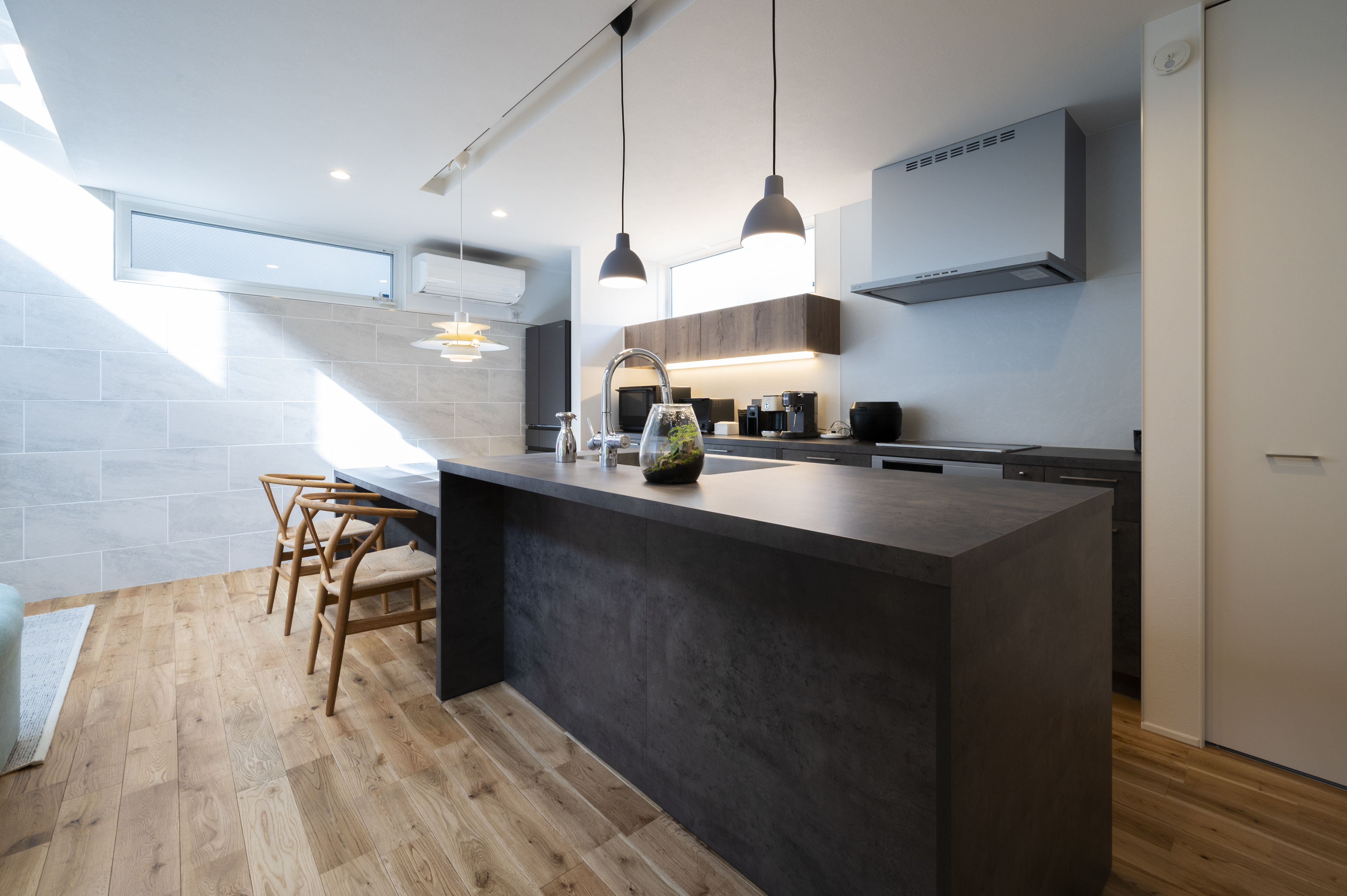 オネストアーク｜ダークカラーのシックなキッチン。広いカウンターとペンダントライトが上質な空間を演出し、料理をすることが楽しくなりそうなデザインである。