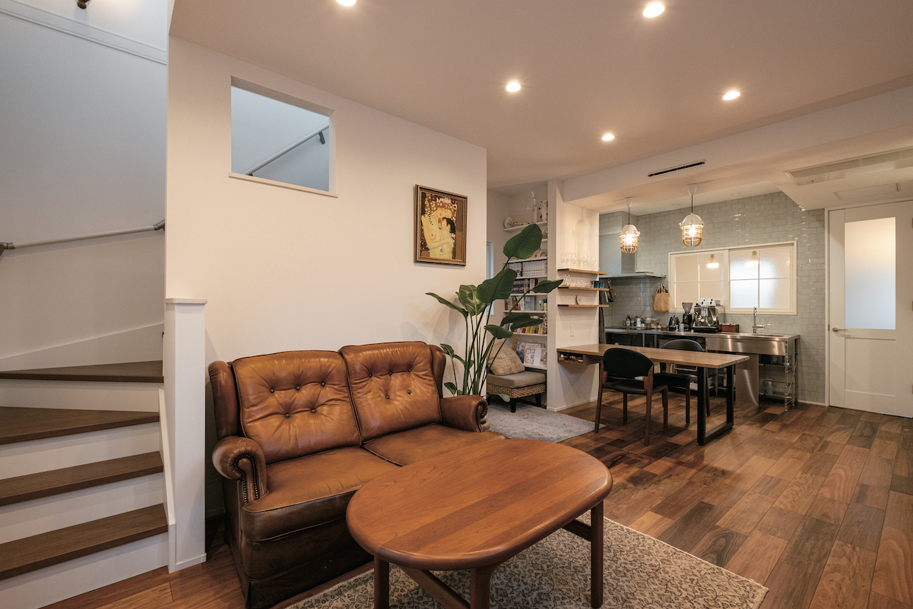 OWN RESORT HOME（オウンリゾートホーム）【1000万円台、デザイン住宅、インテリア】ソファとテーブルは定額に含まれ、Sさんが直感で選んだそう。壁に開けた内窓が階段の吹き抜けから1階に光を運ぶ。ダイニングテーブルは壁に付けて造作し、床の色に合わせて塗装。その横に本棚を造作した