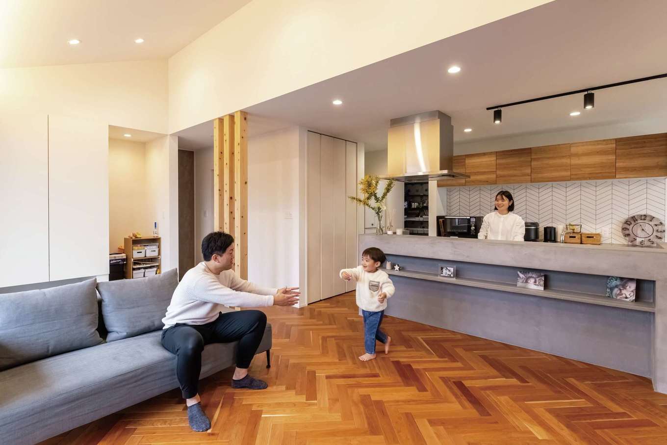 HAPPY HOUSE（山田工務店）【デザイン住宅、間取り、平屋】暮らしの中心となるLDK。キッチンに立つ奥さまの視線の先には、家族がくつろいだり子どもが元気に遊んだりするリビング、さらに大きな窓越しに四季の花が彩る庭の景色が広がる。足元には雑誌で見て憧れていたヘリンボーン床を敷き詰めた