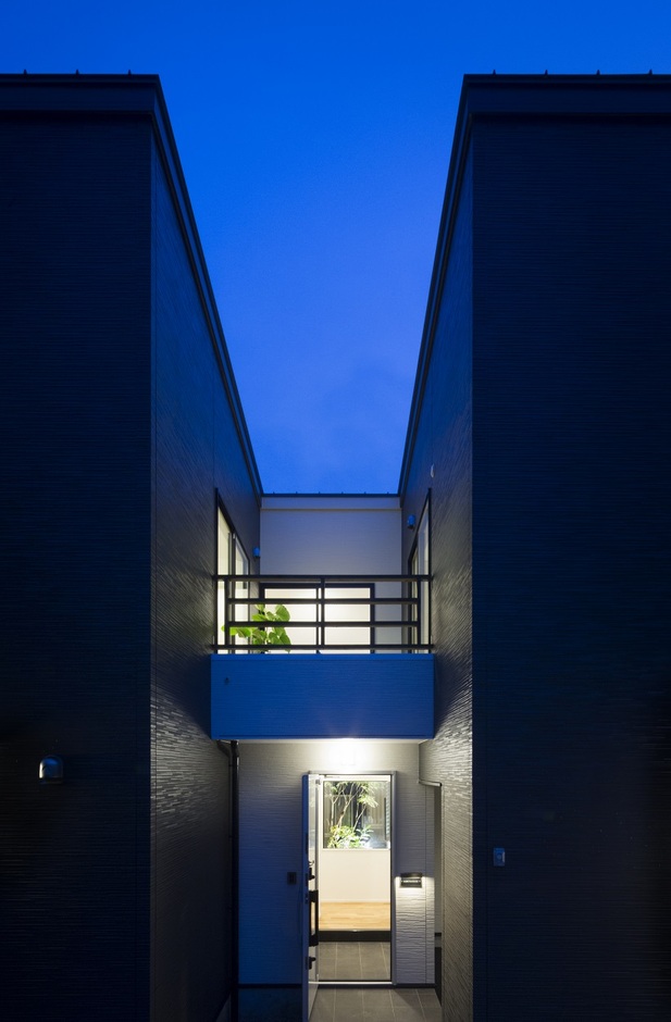 玄関アプローチの夕景。2つの箱に挟まれたスリット状の空間から、内部空間に導かれるデザイン。玄関に入っても光庭があるため、閉鎖感を感じない。玄関上部は子どもバルコニーになっている
