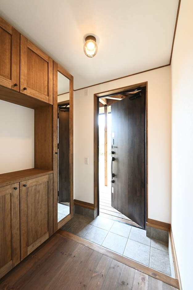 木製の収納とシンプルな照明が調和する、温かみを感じる玄関スペース。外光を取り入れ、明るさも確保されている。