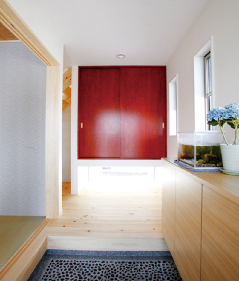玄関奥の収納扉は、センの板の染色染め。白い天井と檜の床に挟まれた赤色がポイントカラーに。ご主人曰く、帰宅したときにホッと心が和むそうだ