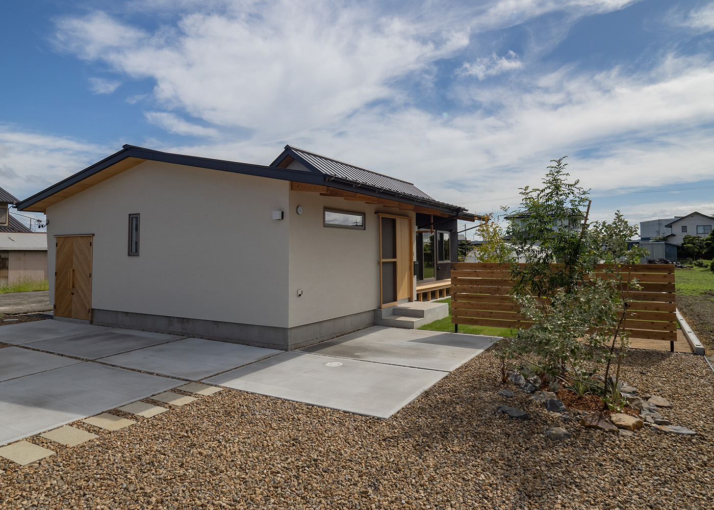 石牧建築【デザイン住宅、子育て、平屋】のどかな住環境にしっとり馴染んだ平屋づくりの外観。塗り壁とガルバリウムの使い分けにより、素材の良さがいっそう引き立てられた。ヘリンボーン柄に施工した外部収納の木製扉も、上品なアクセントを添えている