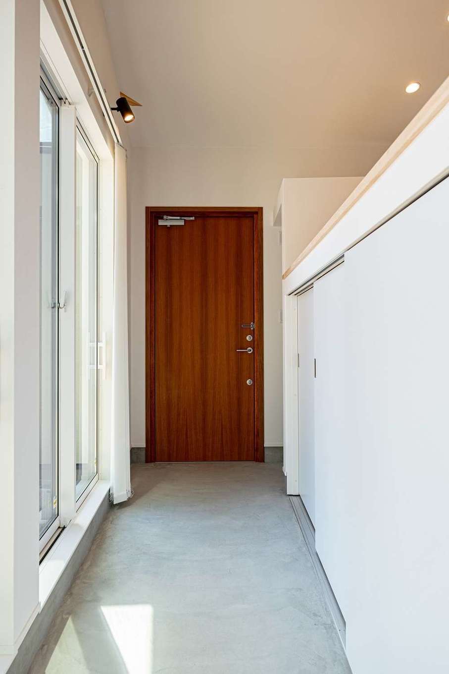 S.CONNECT（エスコネクト）【デザイン住宅、建築家、平屋】無垢の玄関ドアを開けると、掃き出し窓に沿って広い土間廊下が続き、行き止まりがダイニングキッチン。白い腰壁の反対側にリビングがある