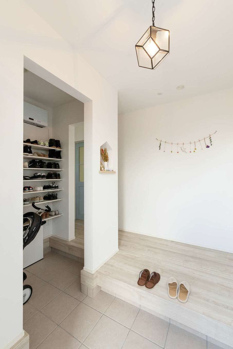 HAPPY HOUSE（山田工務店）【デザイン住宅、子育て、間取り】玄関は家型のニッチとチラリと見えるお気に入りのブルーのドアがアクセント。家族用の玄関を兼ねた機能的なシューズクロークを備え、いつもキレイが保たれる
