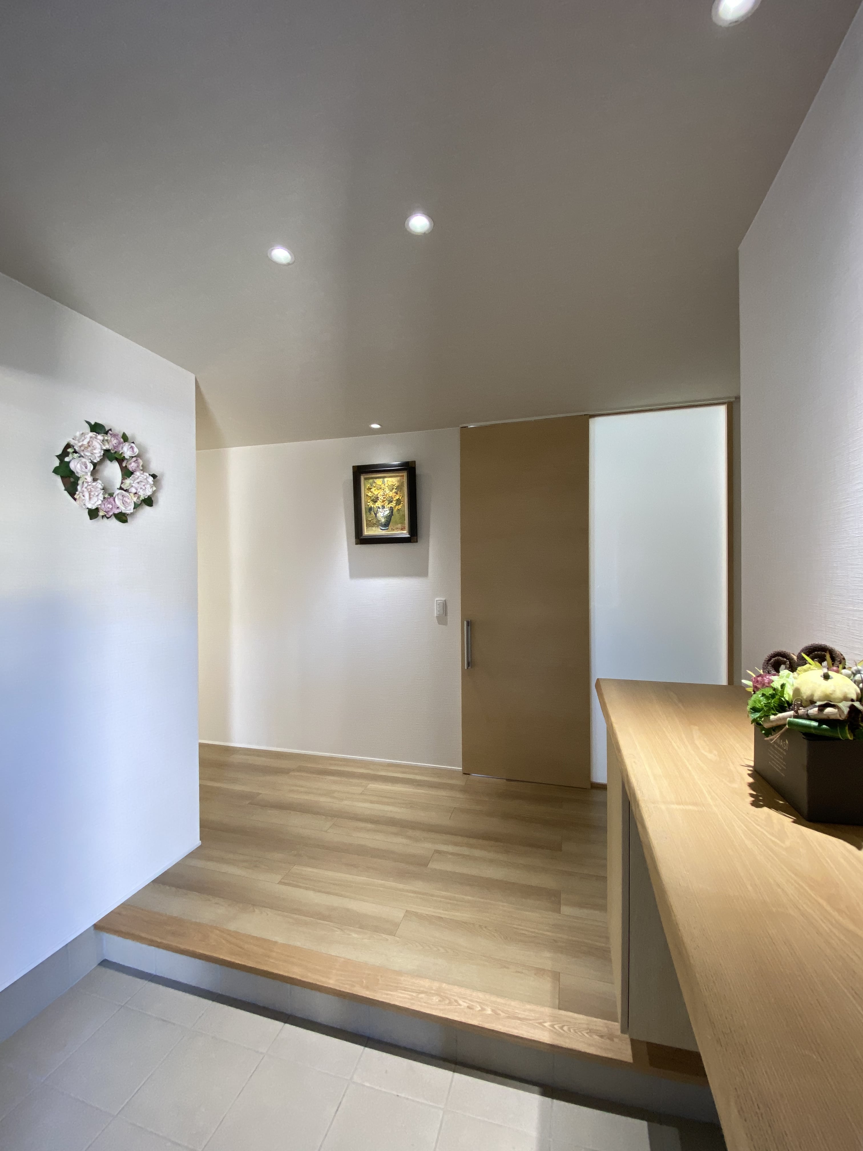 安田住宅｜安田建築設計室｜白を基調とした広々とした玄関ホール。壁に飾られたアートや花のディスプレイが、訪れる人を優雅に迎える雰囲気を演出している。