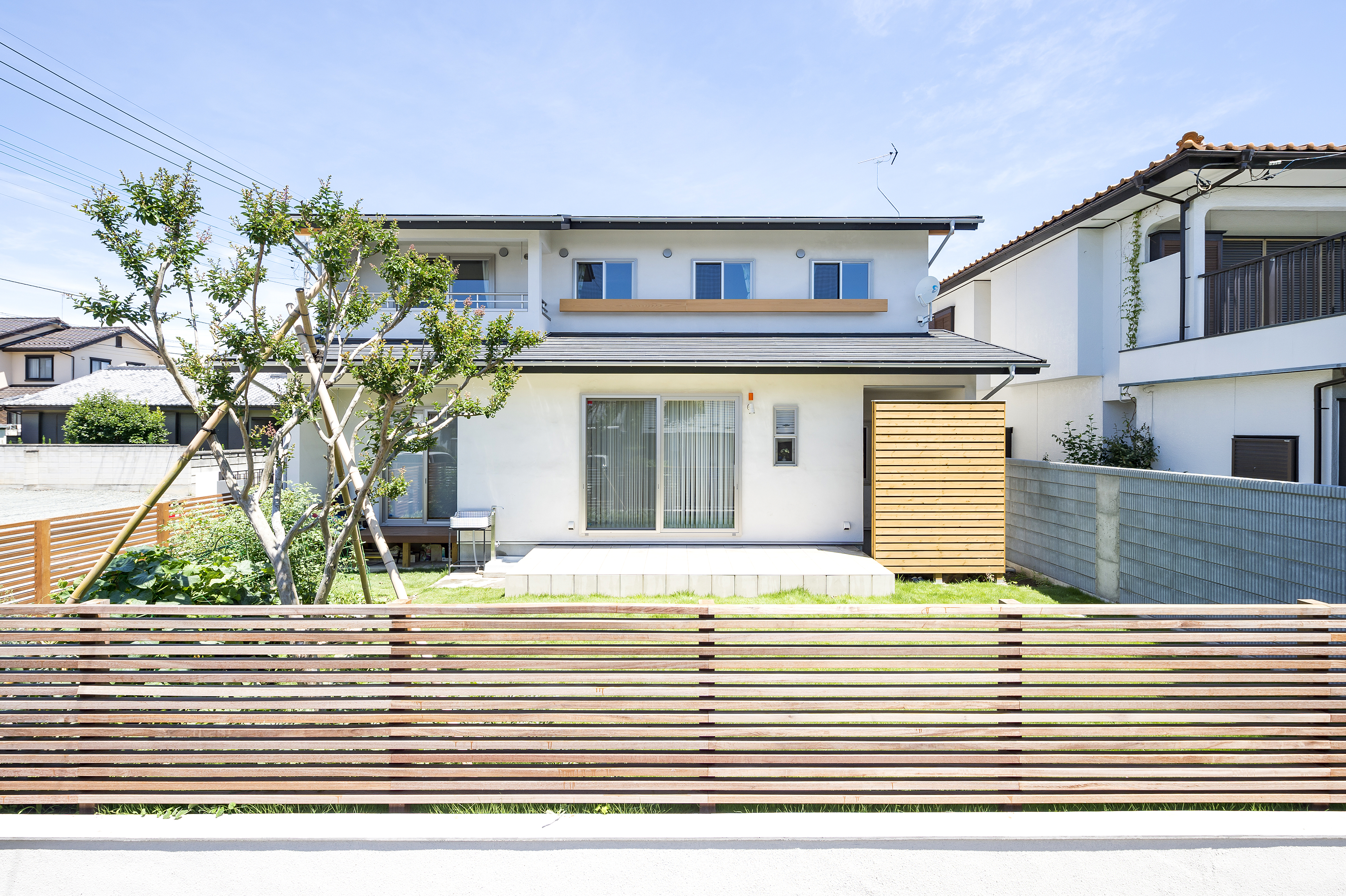 しあわせの住まい一級建築士事務所｜木製フェンスが印象的な二階建て住宅の外観。庭の緑と調和し、リラックスした雰囲気を演出している。