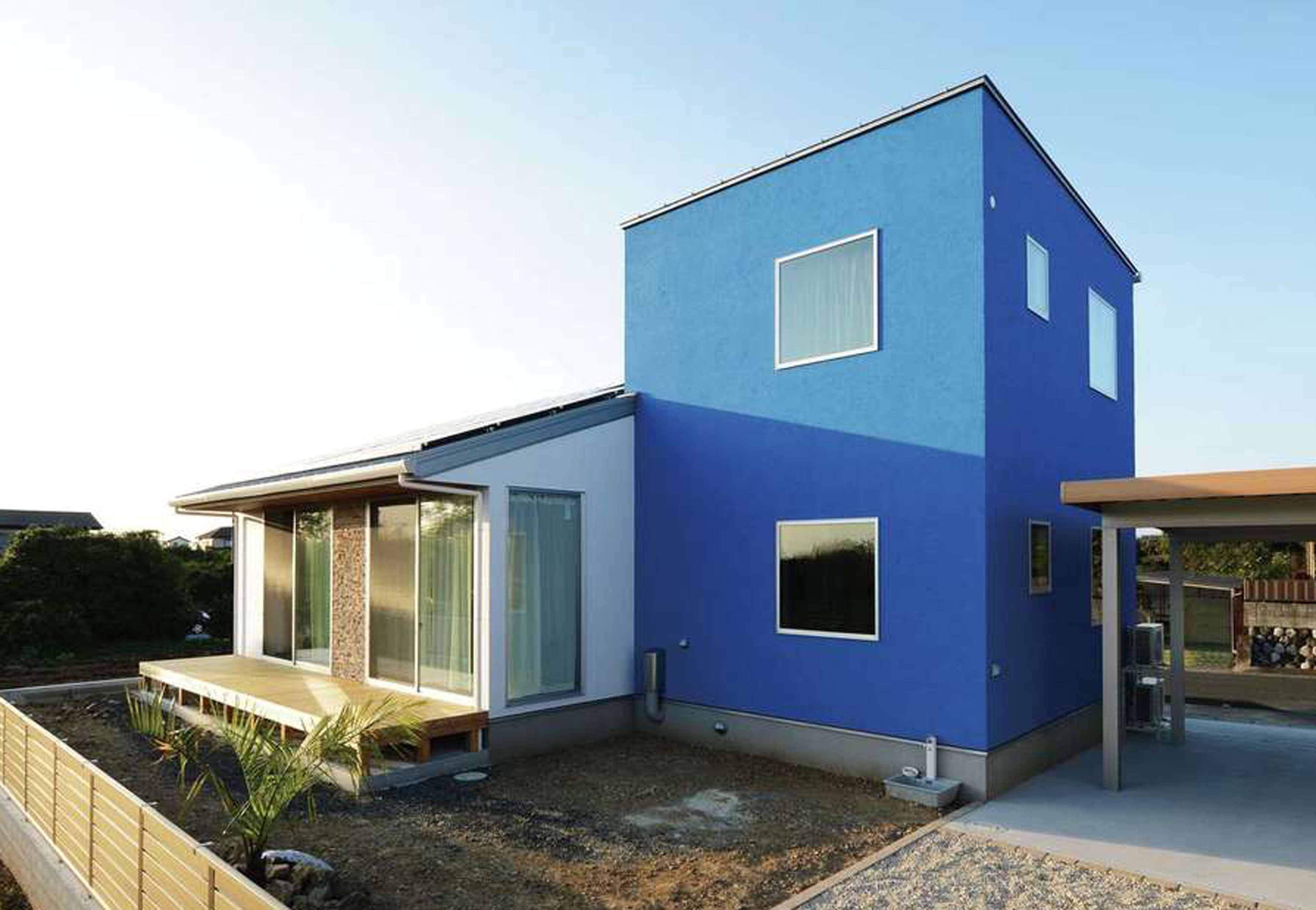 Yamaguchi Design 【デザイン住宅、省エネ、インテリア】コバルトブルーと白を組み合わせた外壁は、遠くからでも目に留まる存在感。コバルトブルーの塗り壁は、色合いを理想の色に調合してもらったオリジナル。南面に開口部を大きく確保してあるので、室内も明るく開放的。庭にはシンボルツリーのヤシの木を植えてある