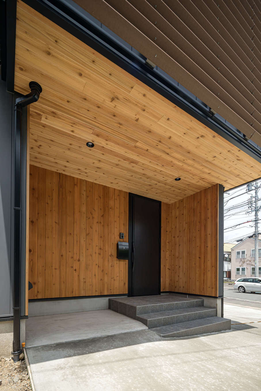 tact design firm【デザイン住宅、間取り、スキップフロア】軒の深い玄関ポーチは、雨の日もストレスフリー。ガルスパンの外壁と無垢材の壁とのコントラストが特徴的