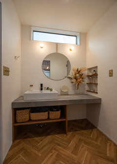 モルタル調のカウンターにベッセルボウルの造作洗面を組み合わせた洗面台。ヘリンボーンの床が空間を調和しつつ、ゴールドのアイテムが華やかさを演出。収納も十分に確保