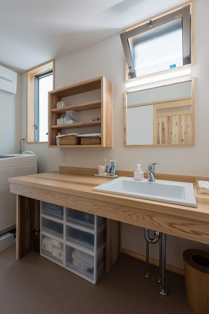 アクトホーム【収納力、自然素材、省エネ】明るい光が差し込む洗面スペース。木製の洗面台と棚が温かみを演出し、シンプルで機能的なデザインとなっている。