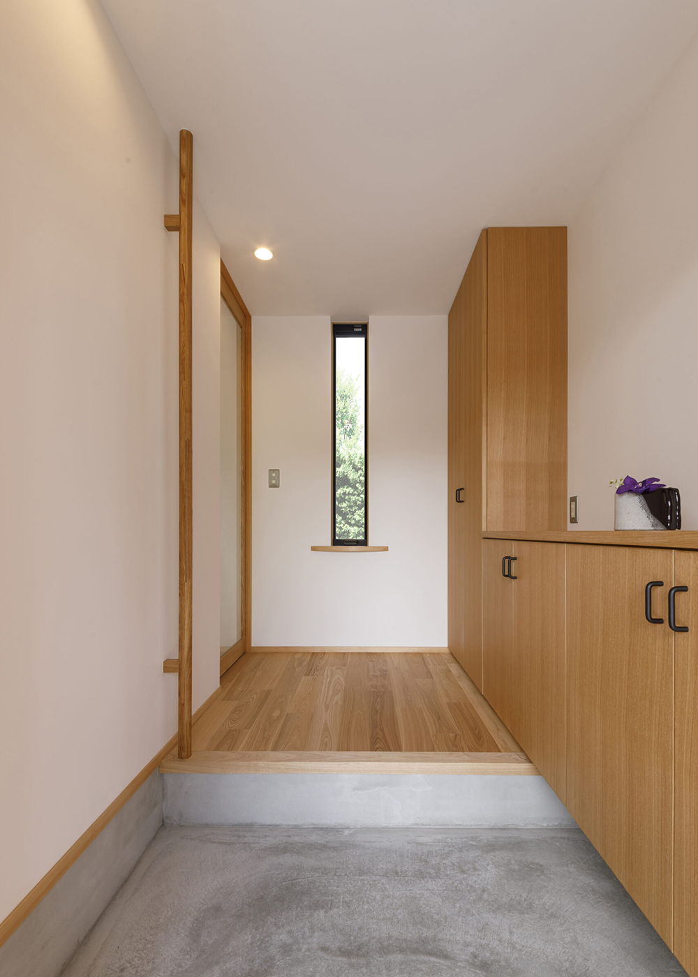 灯建築舎【デザイン住宅、自然素材、省エネ】モルタル仕上げの玄関は、無垢の床や造作の収納とも相性がいい。正面の窓には借景のグリーン。その下にはディスプレイ用の棚も設置してもらった。左手LDK入口の建具は、二重のガラスの間に天然の織布をはさんだオリジナル