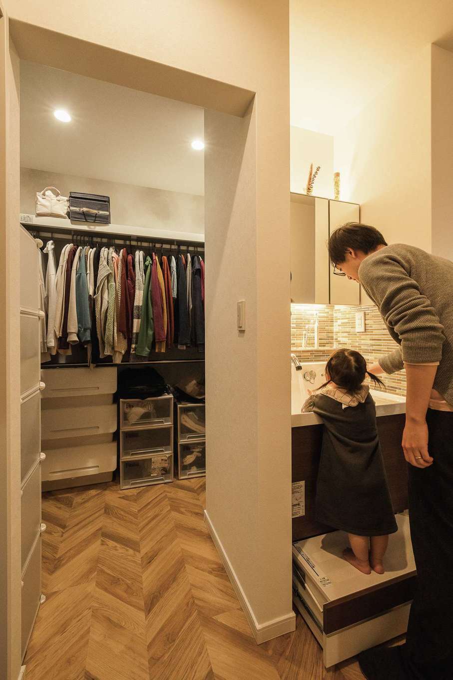 三和建設【デザイン住宅、子育て、間取り】脱衣室と離したかった手洗いコーナーは、キッチンの手前に設置。娘さんが自分で手を洗えるよう練習中だ。奥はファミリークローゼット。ヘリンボーン柄のフローリングが高級感を演出する