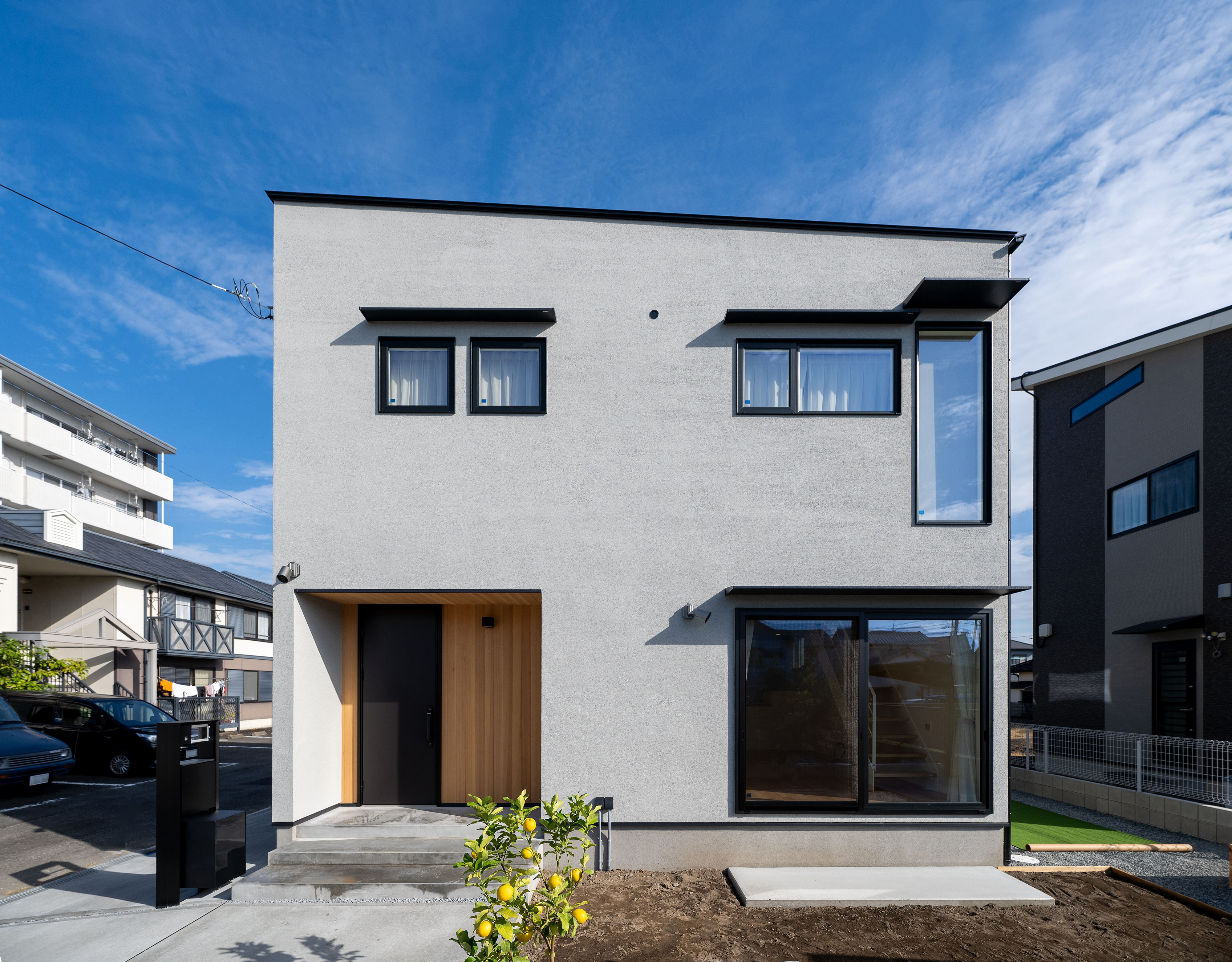 ハウスプラン（R＋house沼津・富士）【デザイン住宅、省エネ、建築家】グレー＆アクセントのブラックの組み合わせによるスタイリッシュさと塗り壁の表情がもたらす穏やかさが調和する。日射に合わせて庇の位置と長さが計画されている