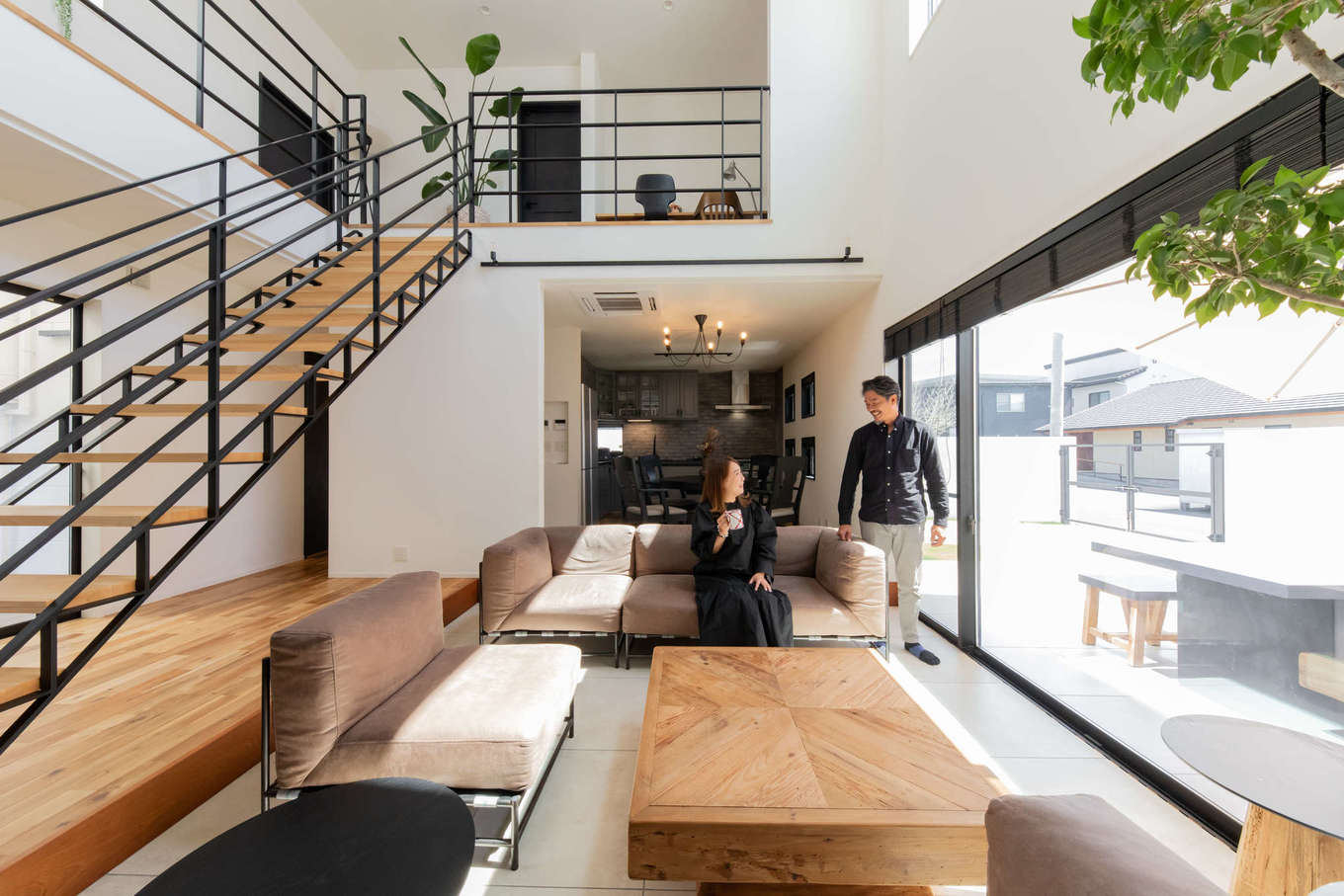 幸和ハウジング【デザイン住宅、夫婦で暮らす、ガレージ】アカシアの無垢の床を用いた室内は、壁を白で統一し、サッシやドアには黒を用いて、上質で洗練された空間を演出。吹き抜けにタイル敷きのダウンフロアを組み合わせたリビングは、天井高がいっそう高く感じられ、大開口からは庭を見渡せる