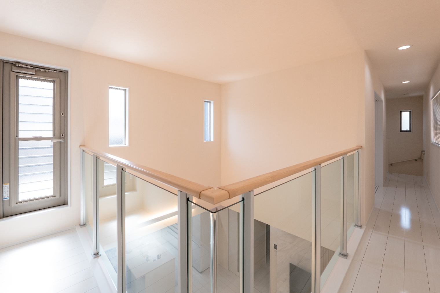 アイダ設計　｜明るい光が差し込む廊下。手すりにはガラスを使用し、視覚的に広がりを感じさせるデザインとなっている。