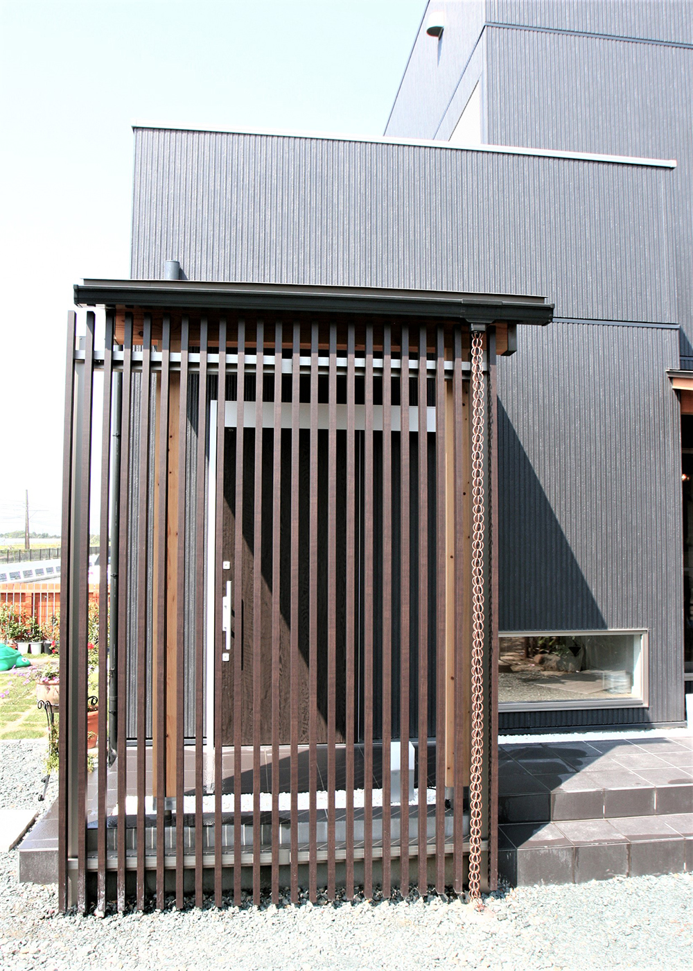丸昇彦坂建設【デザイン住宅、収納力、和風】黒の外装に縦格子とモダン溢れるデザイン。格子の木と玉砂利、鎖樋が古き良き庭園の顔を思わせる