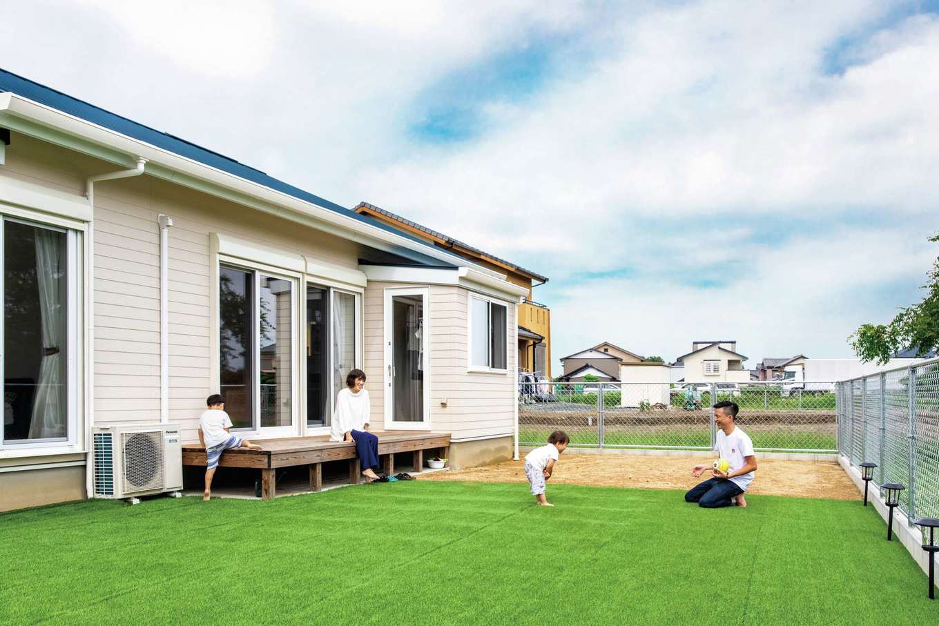 水田建設【デザイン住宅、省エネ、平屋】人工芝を敷き詰めた庭で子どもと遊ぶひととき。ウッドデッキが内と外をつなぎ、庭がいっそう身近に感じられる