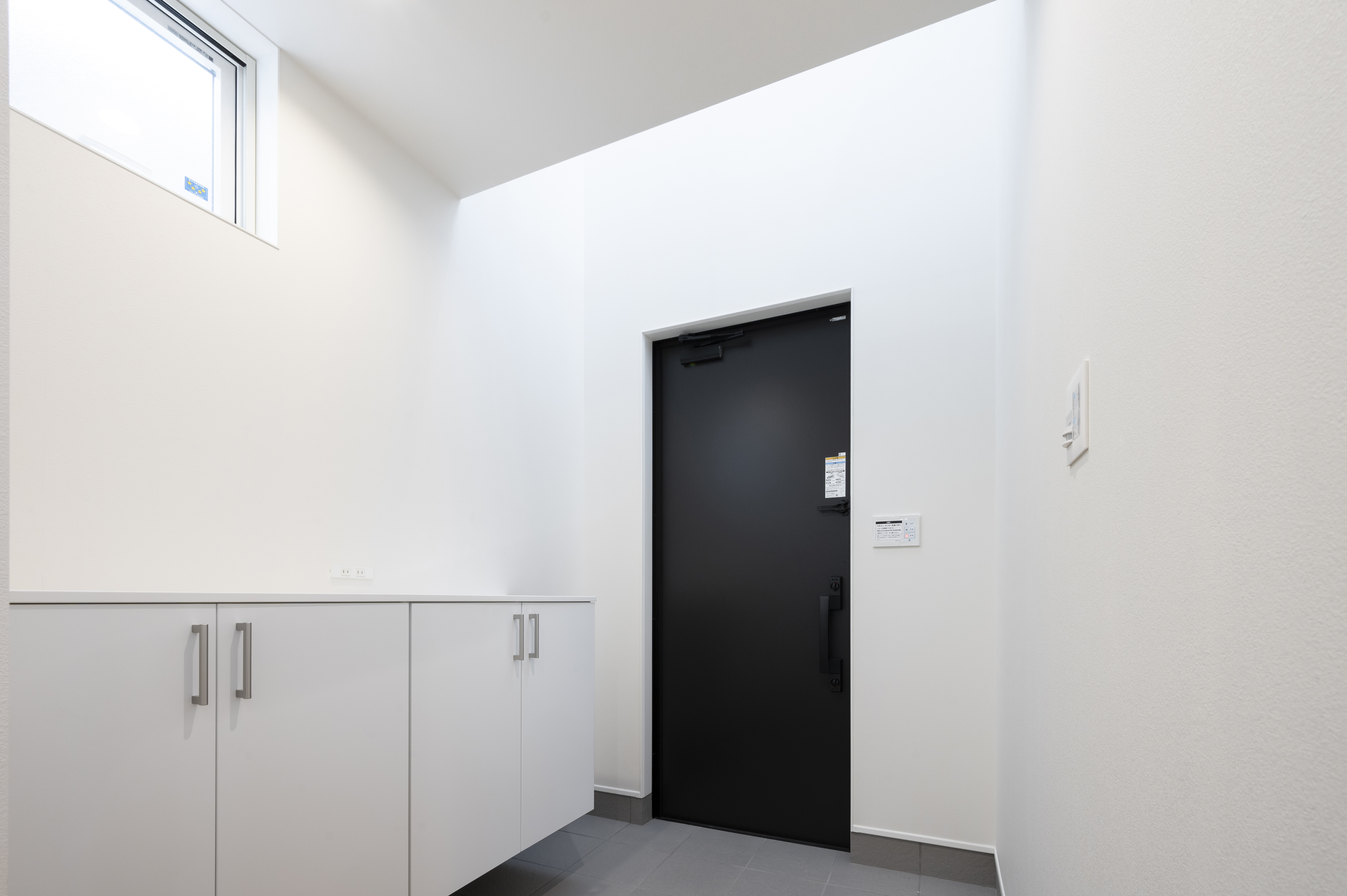 オネストアーク｜シンプルでモダンなデザインの玄関スペース。白を基調とした空間に、黒いドアがアクセントとなり、スタイリッシュな印象を与えている。