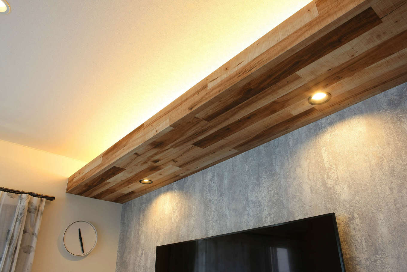 ハート住いる｜テレビの上の梁の上下に間接照明を埋め込み、木目調のクロスを巻いてニュアンスを出した