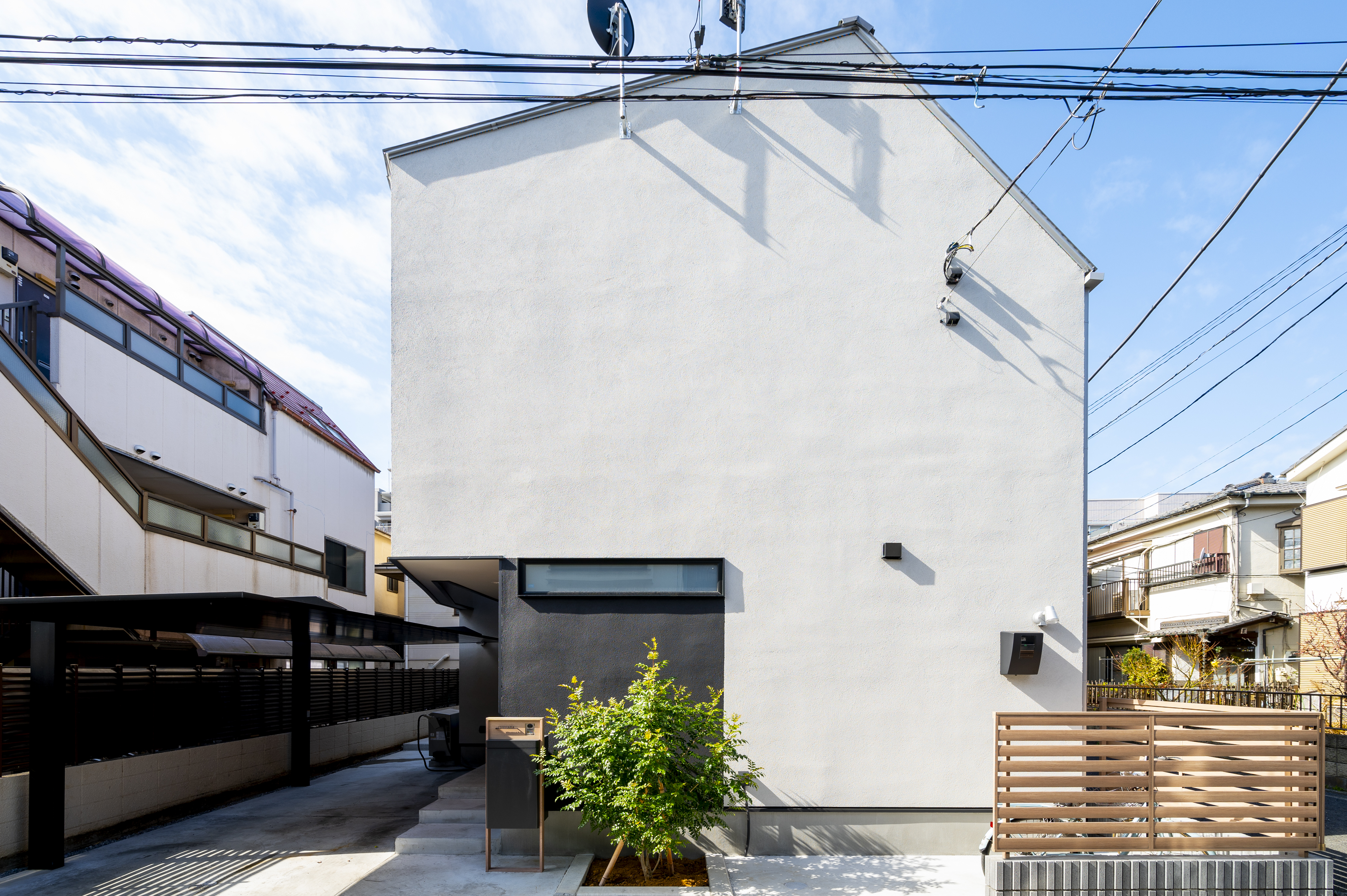 オネストアーク｜シンプルでモダンな外観を持つ住宅。白い壁と木製フェンスが調和し、落ち着いた雰囲気を醸し出している。住宅街に溶け込みながらも個性を主張するデザイン。