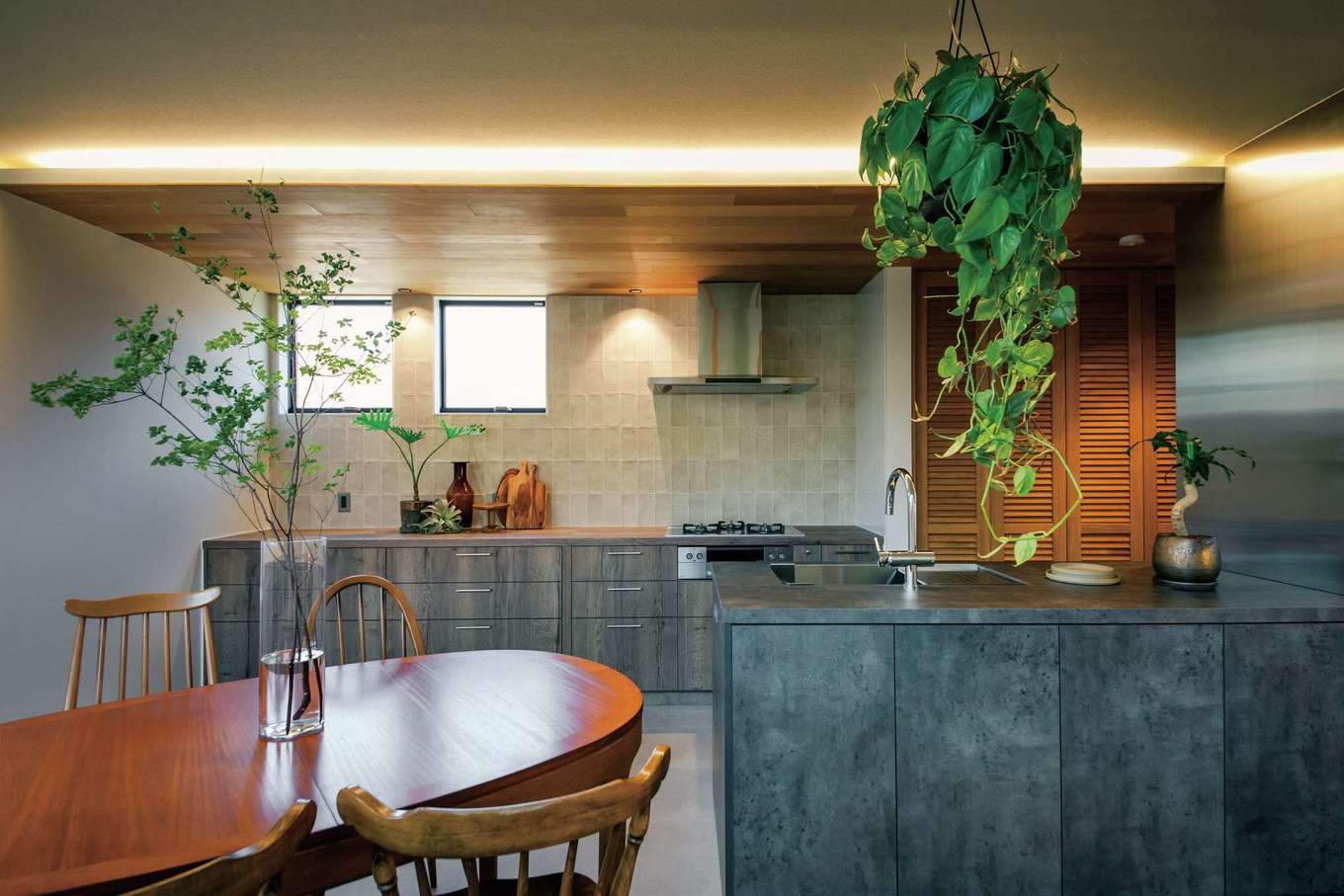 住家 JYUKA【デザイン住宅、間取り、インテリア】DKは間接照明を施した無垢の下がり天井、あえて縦張りにしたタイル、ステンレス製の壁といった異素材を組み合わせ、スタイリッシュかつシックにまとめられている