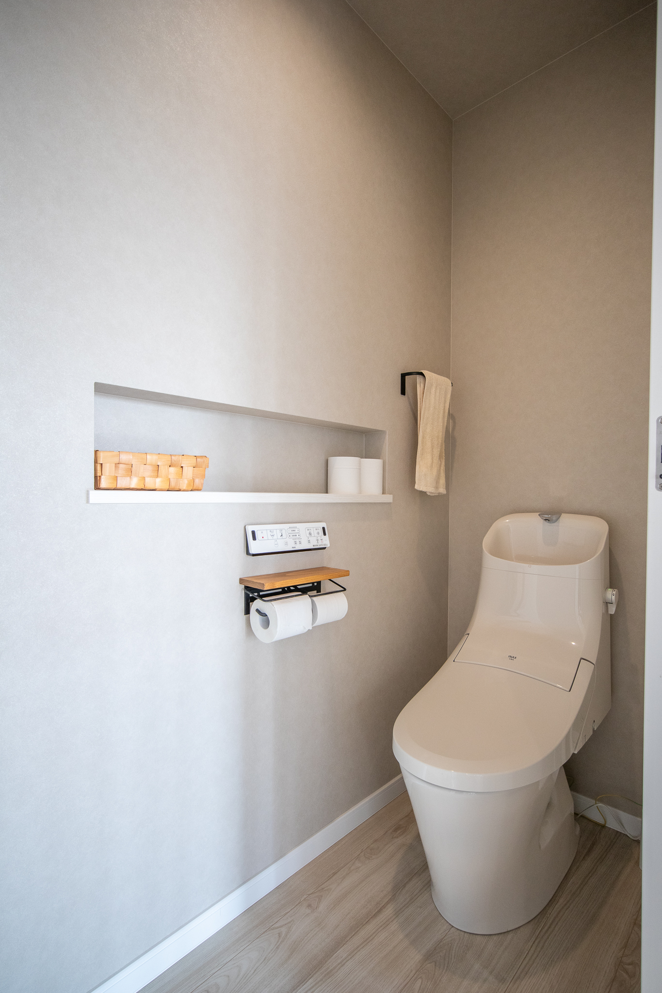コンチネンタルホーム｜シンプルで機能的なトイレ空間。壁には便利な棚が設けられ、トイレットペーパーなどの収納に最適である。白を基調とした清潔感のあるデザイン。
