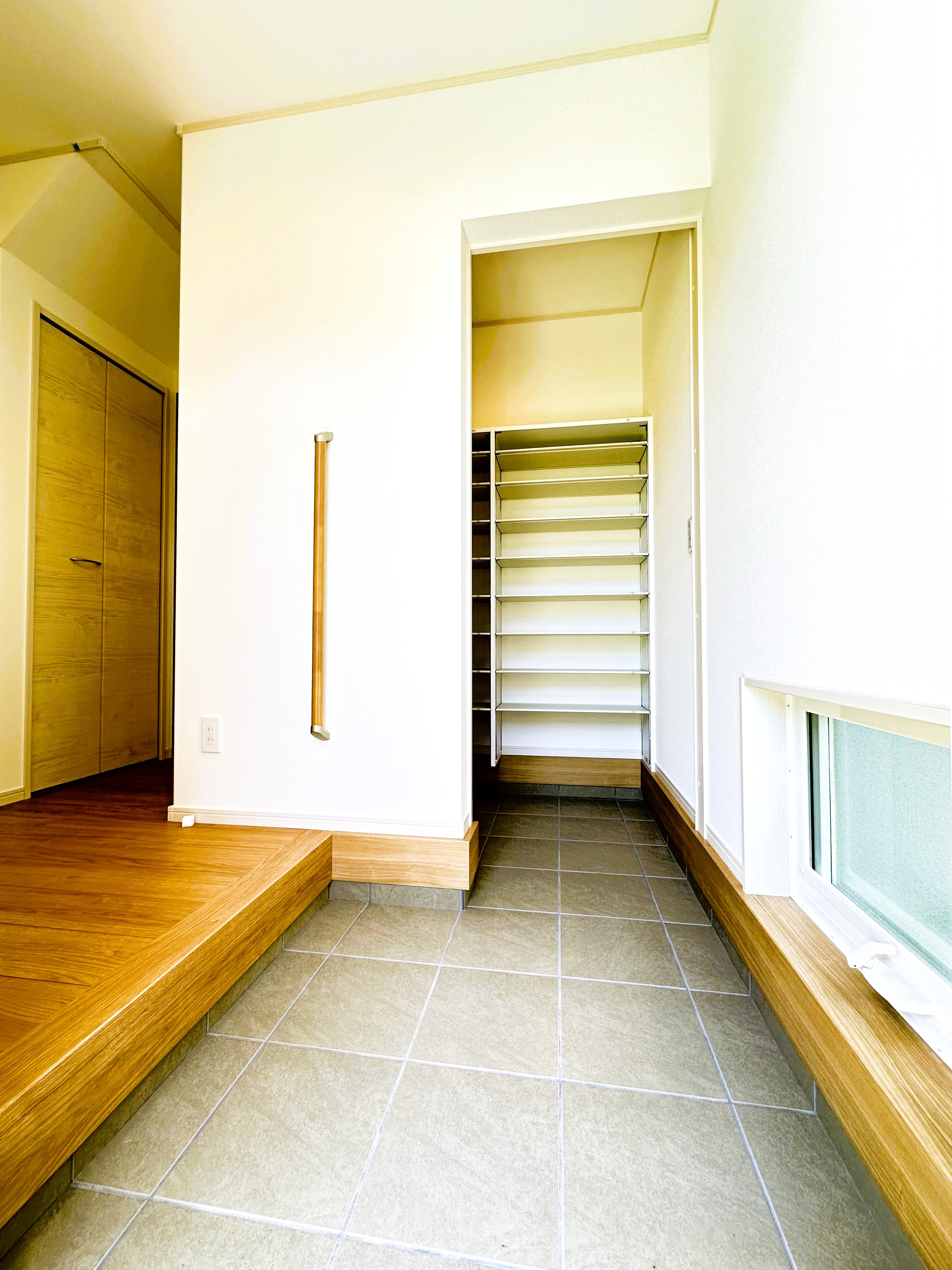 イシカワ 岐阜支店｜明るい玄関土間は、シンプルかつ機能的なデザインで統一されている。タイル張りの床がモダンな雰囲気を演出。目隠しにもなる扉の奥は広い収納があり機能的。