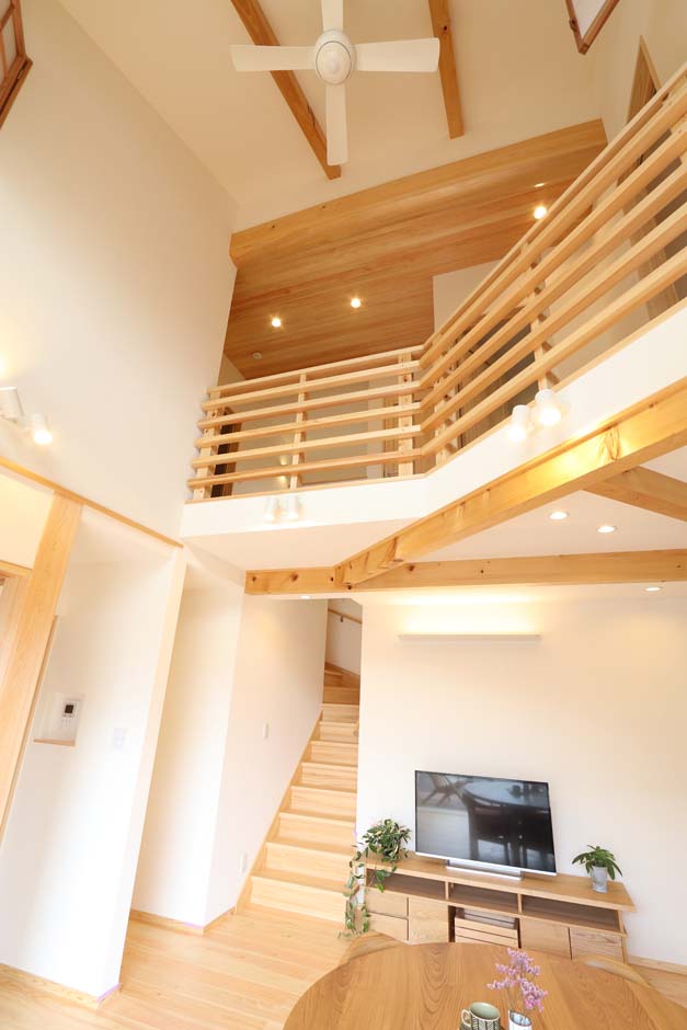 エコフィールド【自然素材、省エネ、間取り】リビング階段と吹き抜けが、1階の住空間と2階の居室とを繋ぐ。見上ゲルト目に入る太鼓梁の丸みが柔らかな雰囲気を醸し出す
