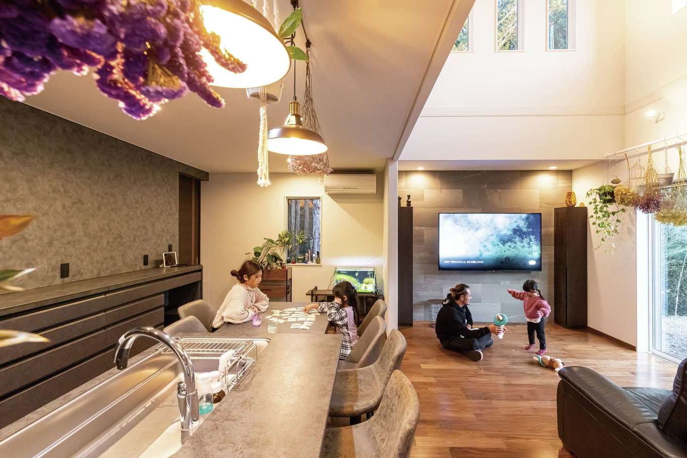 住宅工房 アリアンス【デザイン住宅、省エネ、間取り】吹抜けの開放感が気持ちいいLDK。天井の高低差でより広く感じられる。夫婦の好きなグレーを空間に取り入れたいと、キッチンの色に合わせてダイニングテーブル、カップボード、壁のクロスを選んだ