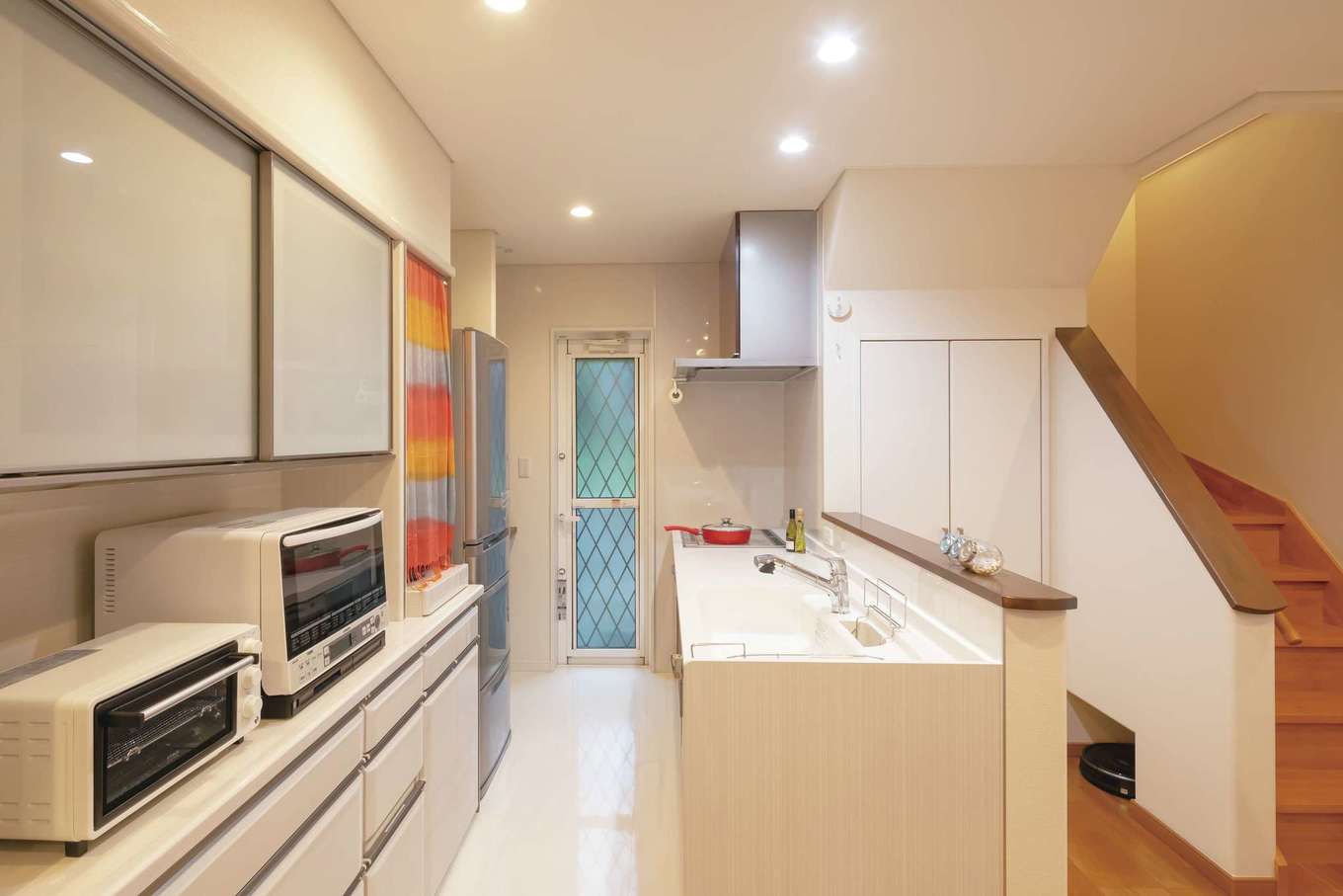 住宅工房 アリアンス【デザイン住宅、趣味、間取り】家族の様子を見渡せるオープンキッチン。生活感を出さないための収納力も充実。子どもたちがママに「ただいま～」と言ってから2階へ上がるリビング階段を採用。階段下にはルンバ基地も！