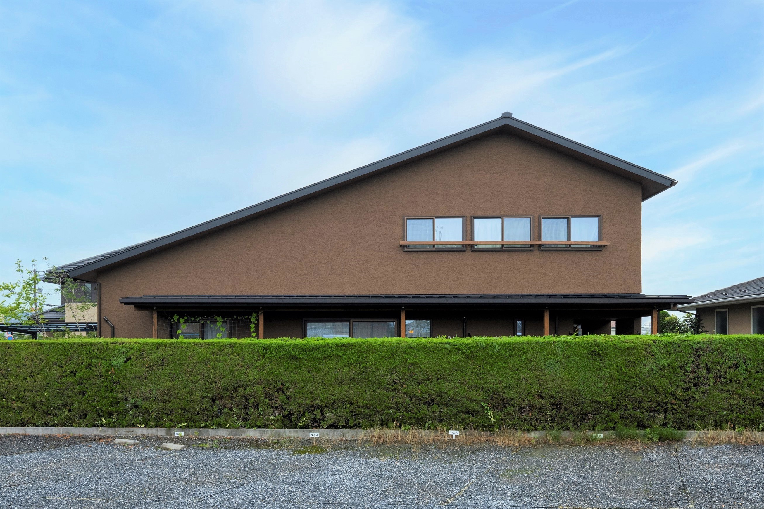 グランハウス一級建築士事務所｜大屋根の茶色の塗り壁のお家。目隠しを兼ねた緑の生垣は以前からあるものを活かして。

