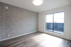 落ち着いたトーンの壁紙とフローリングが特徴の居室。大きな窓から自然光が差し込み、明るく開放的な空間を演出している。