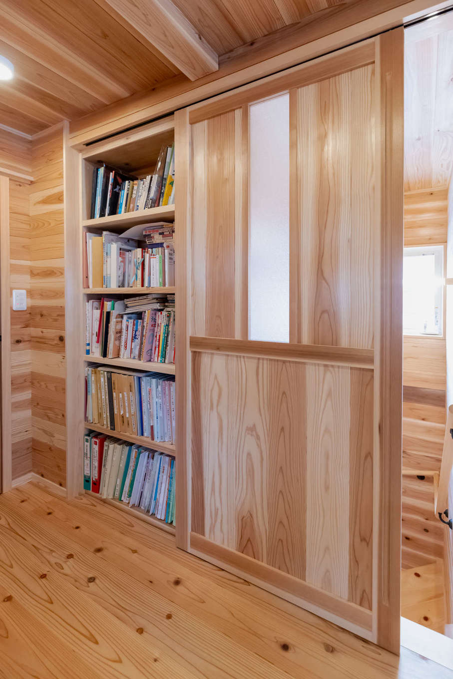 有吉住宅【収納力、自然素材、間取り】2階のホールに本棚を造作。階段のスライドドアを開けると、本棚が隠れる仕掛けになっている