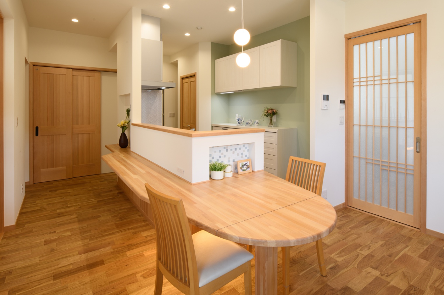 Sus∞Eco Home（サスエコホーム）｜温かみのある木製テーブルを中心にしたダイニング。柔らかな照明とともに、リラックスした食事の空間を演出している。
