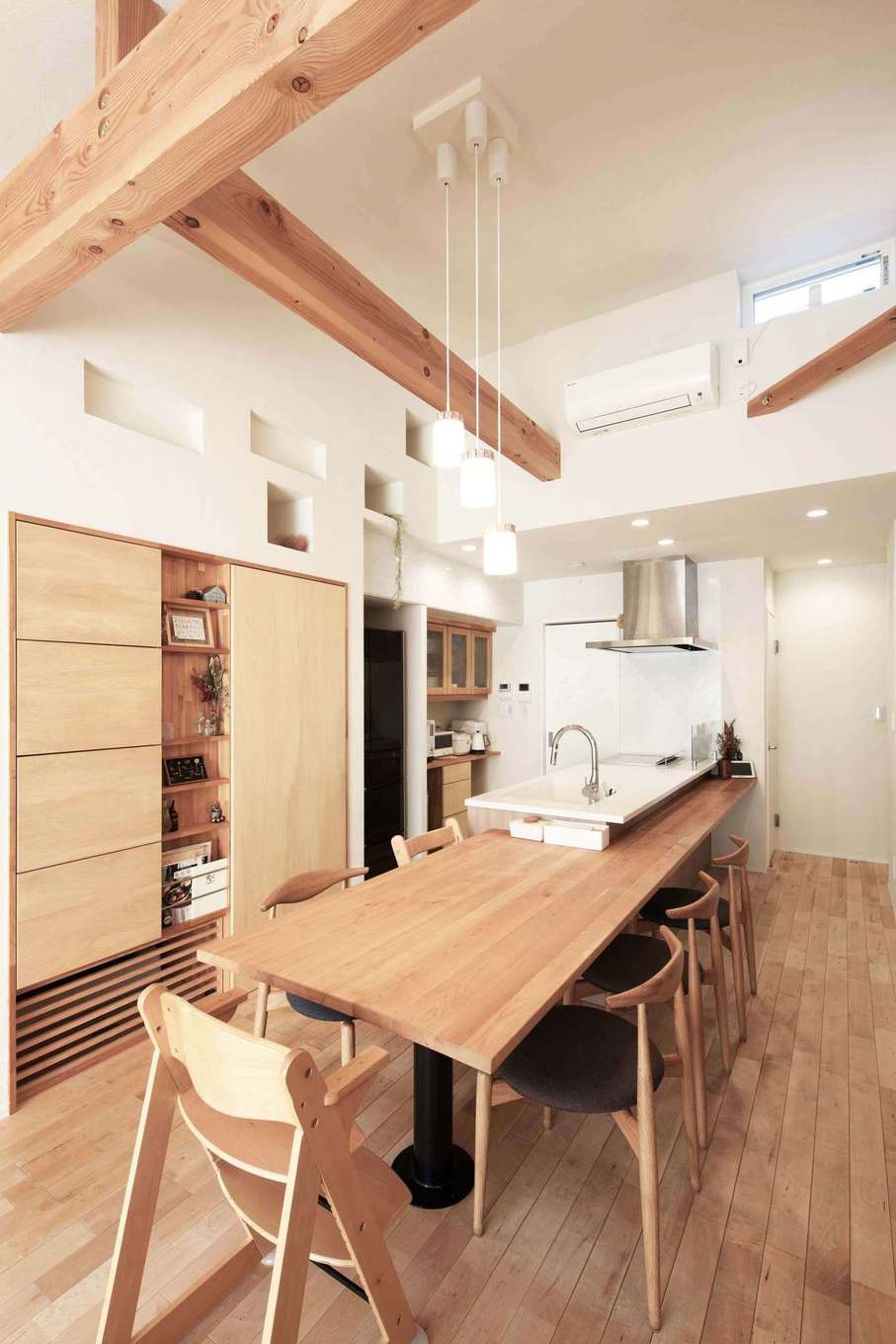 平屋建築ブルーハウス【デザイン住宅、子育て、平屋】キッチンの周りには造作のカウンターテーブルを設け、配膳や片付けが便利に。ダイニングの壁面収納は、小物を飾って楽しむ「見せる収納」と、生活用品を「隠す収納」のどちらにも使えるように工夫されている。壁の上部には夫妻のアイデアでニッチを設け、グリーンを飾れるようにした