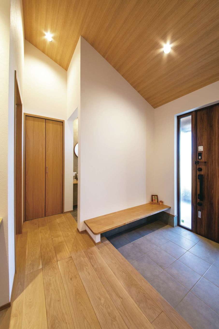 コットンハウス【子育て、二世帯住宅、省エネ】勾配天井でより広く感じる二世帯共有の玄関ホール。木のベンチは両親にも子どもたちにもやさしくて便利