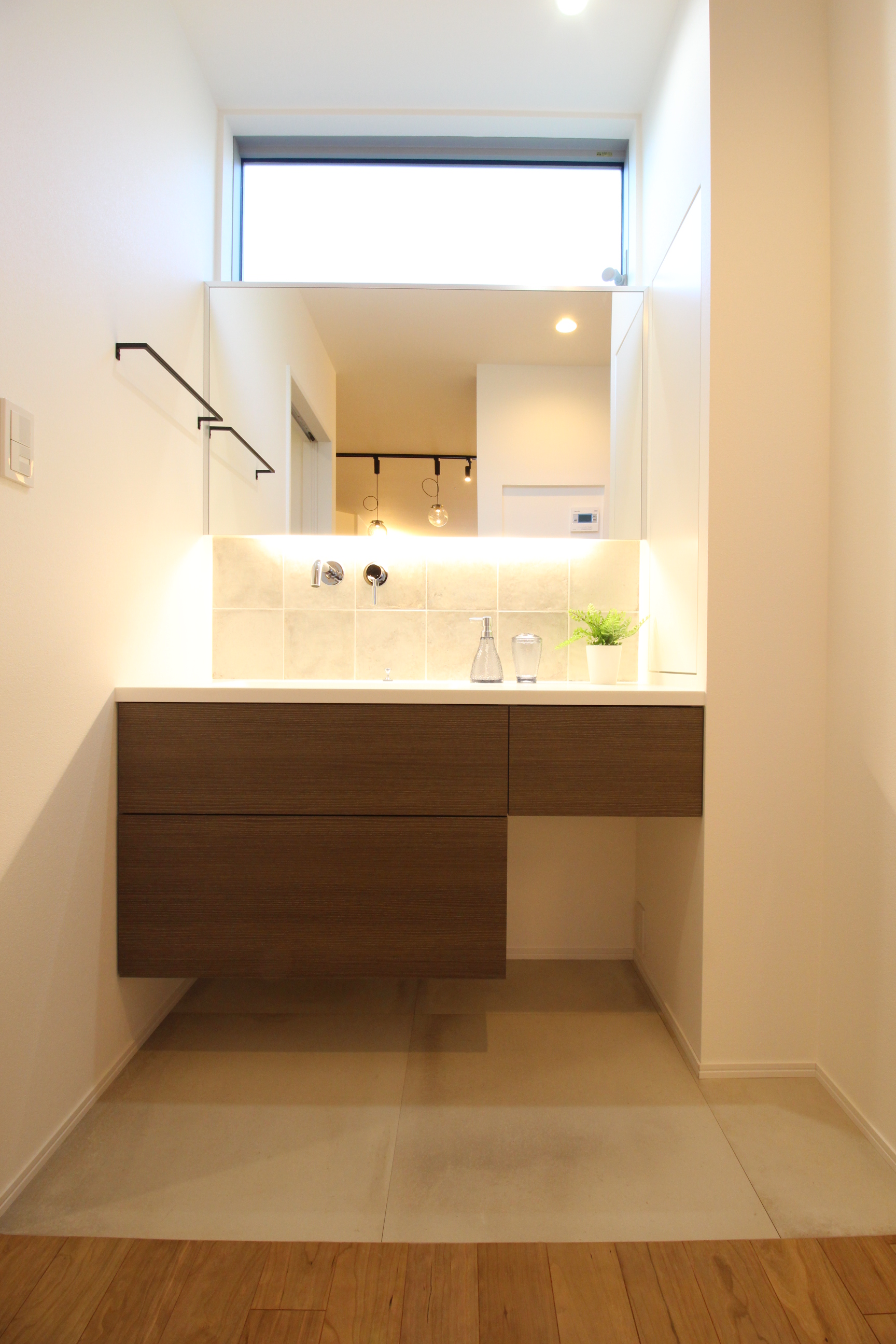 小野田産業～designers house project～｜清潔感あふれる洗面スペース。大きな鏡と明るい照明が使いやすさを引き立てており、シンプルでスタイリッシュなデザインが特徴的である。