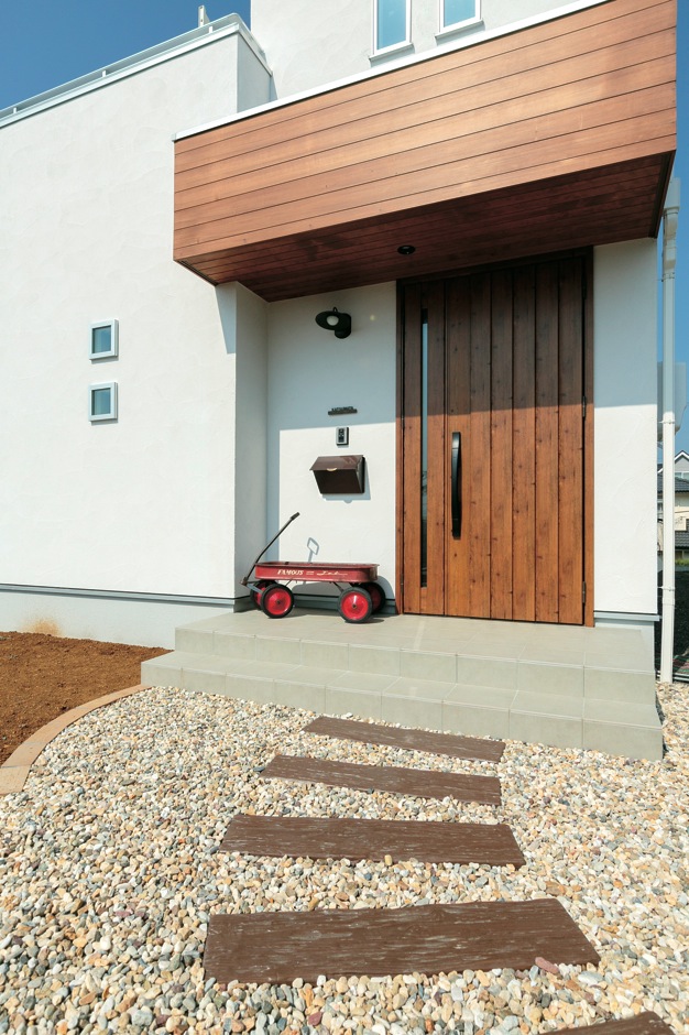 アトリエサクラ【子育て、省エネ、間取り】玄関の上に張り出した木のポーチ屋根が白い塗り壁の外観にぬくもりを添える