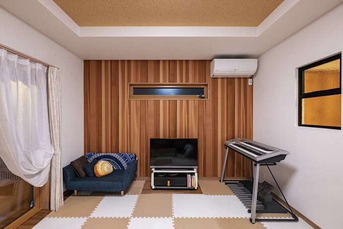 リビングの一面に張られたウッドパネルが空間のアクセントに。室内窓が階段ホールに光を届けつつ、上り下りの気配を伝える