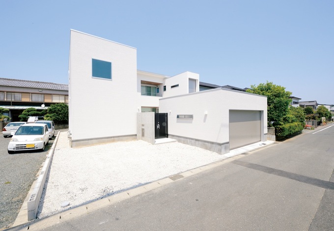 キューブが積み重なったようなモダンな外観。コンクリート打ちっ放しの玄関壁に背の高い門扉がプライバシーを守る