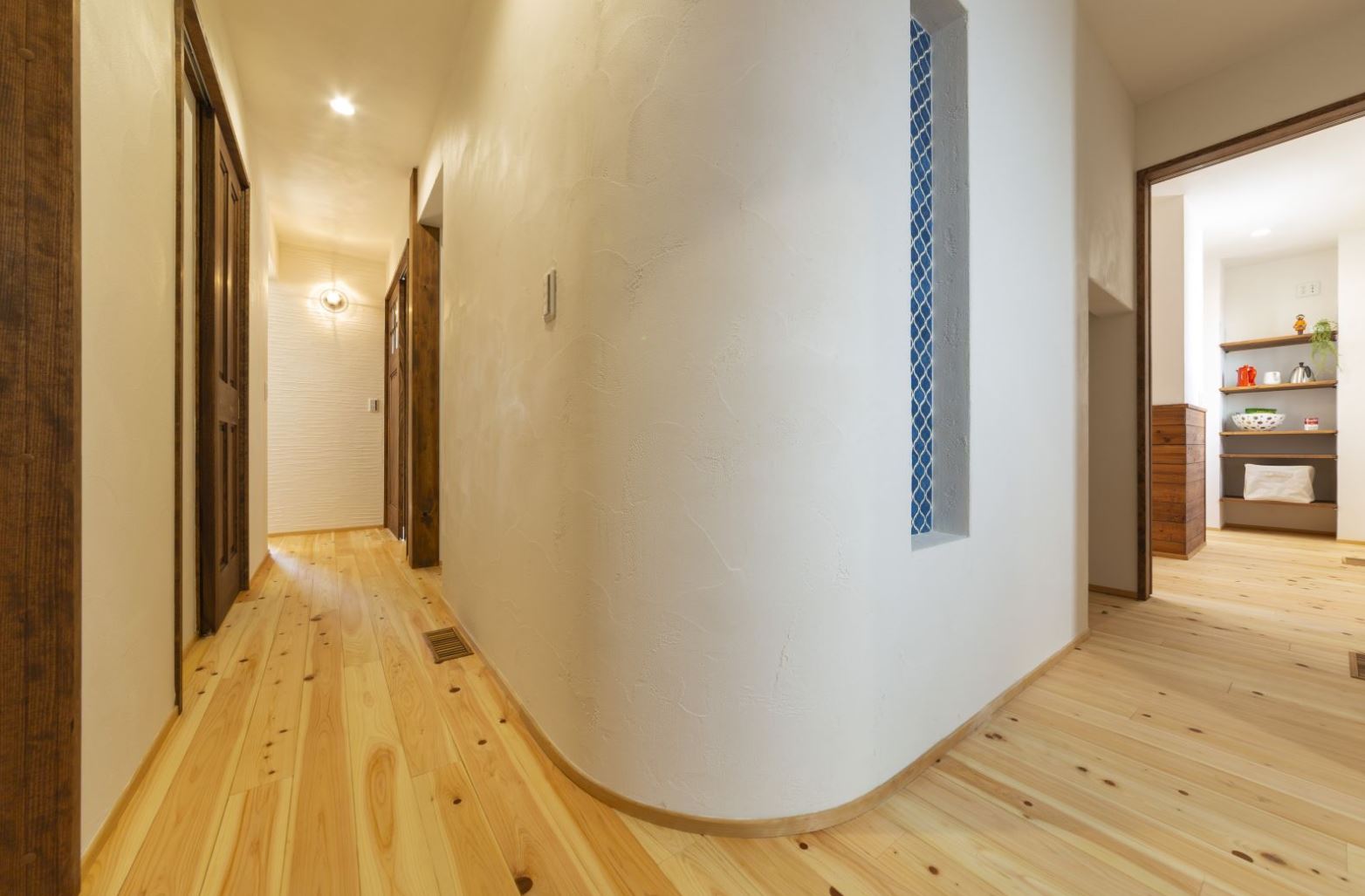 アイジースタイルハウス【収納力、自然素材、間取り】玄関を上がってホールに設けた3畳のウォークインクローゼット。壁をアールにしたことで、空間にやさしさが生まれた。ニッチの青いモザイクタイルがアクセントに。右に進むとダイニングキッチン、左に進むと水回りへとつながる