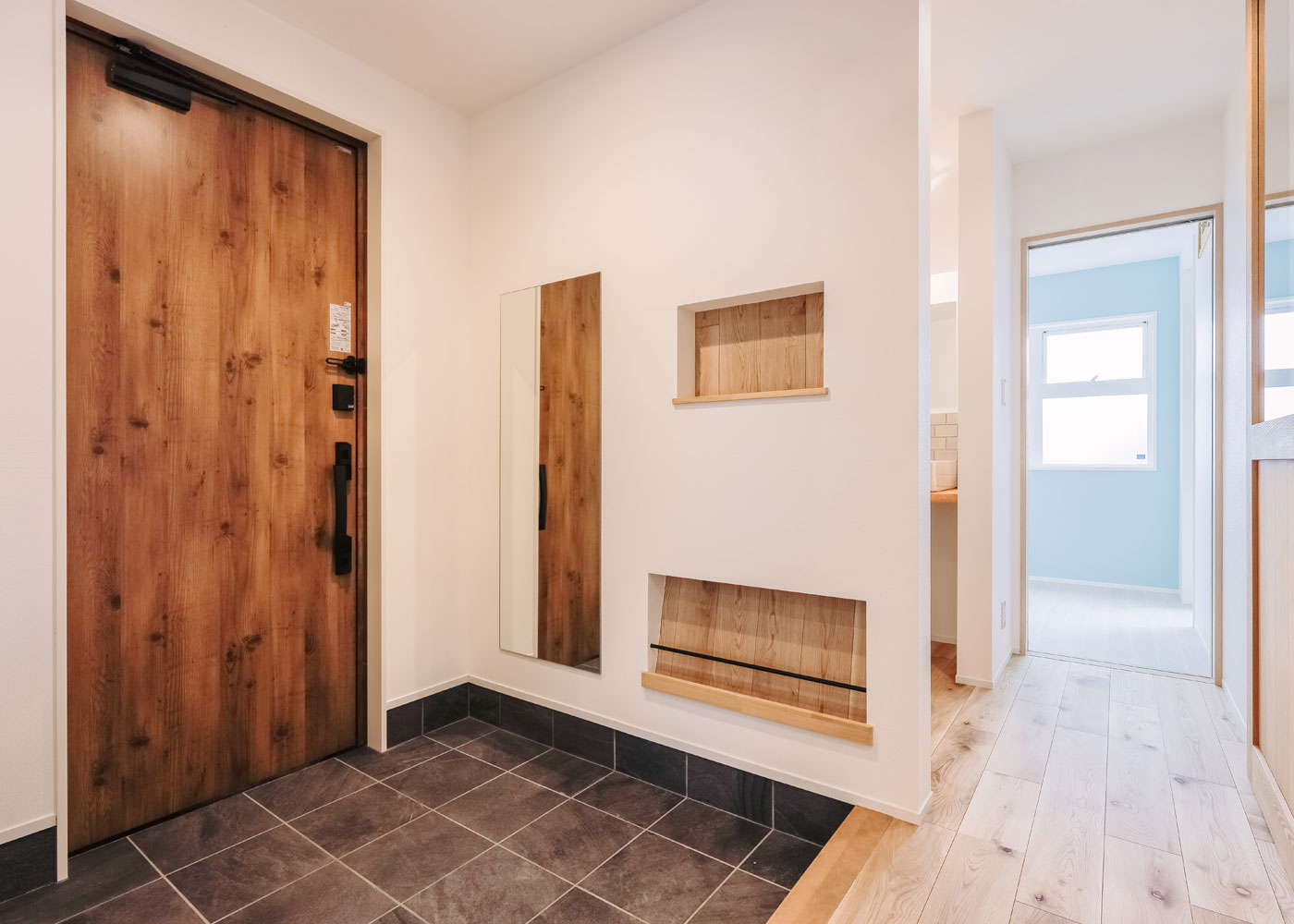 彩羽工藝舎【デザイン住宅、間取り、平屋】玄関は土間部分を広く取り、アウトドアグッズなど外で使うものを仮置きできる。造作したニッチには、小物やスリッパなどを収納。床材は1階・2階ともに無垢材とフローリングのハイブリット材を使用。暖かみと掃除のしやすさを両立