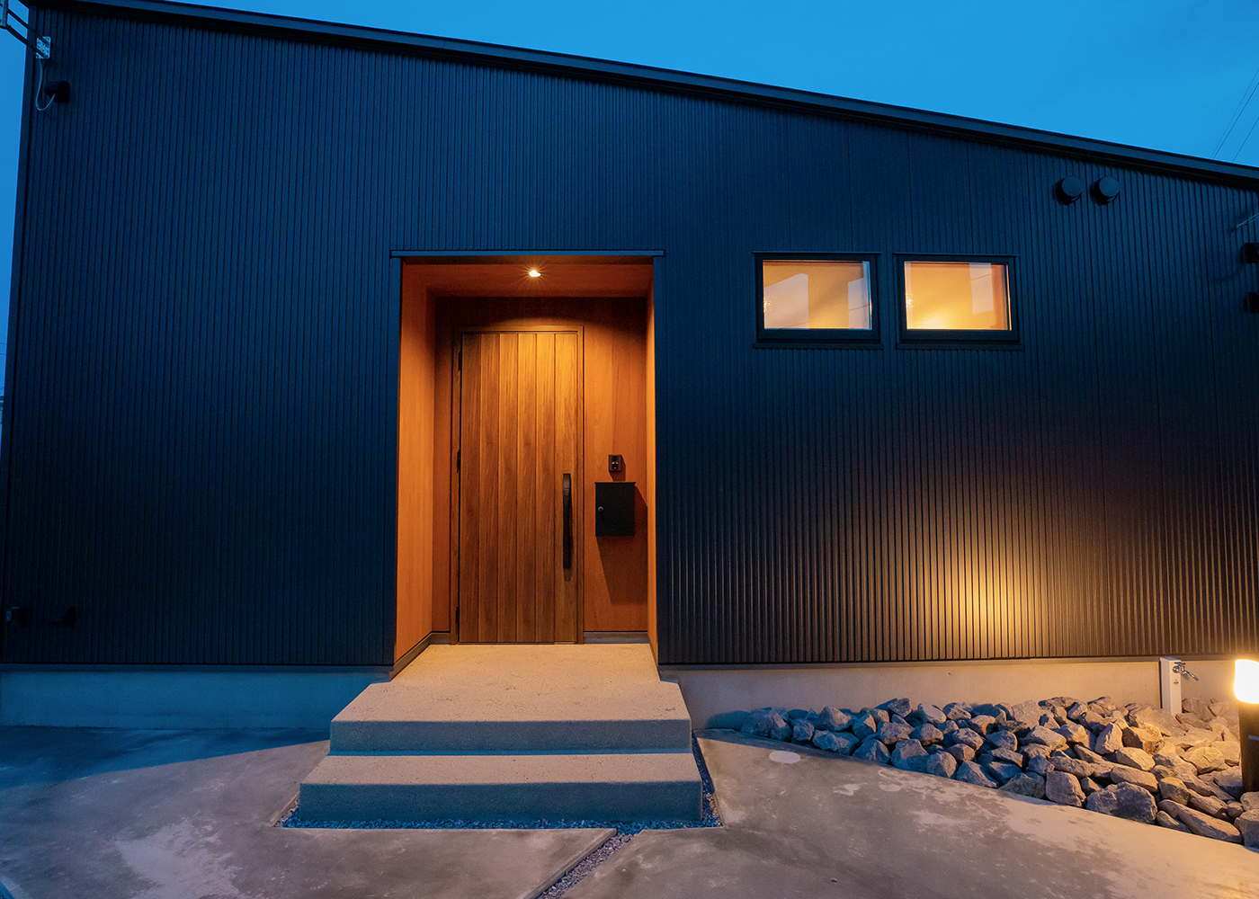 タツホーム・竜建｜シンプルでモダンなデザインの平屋の外観。夜のライトアップが建物の落ち着いた雰囲気を引き立てる。