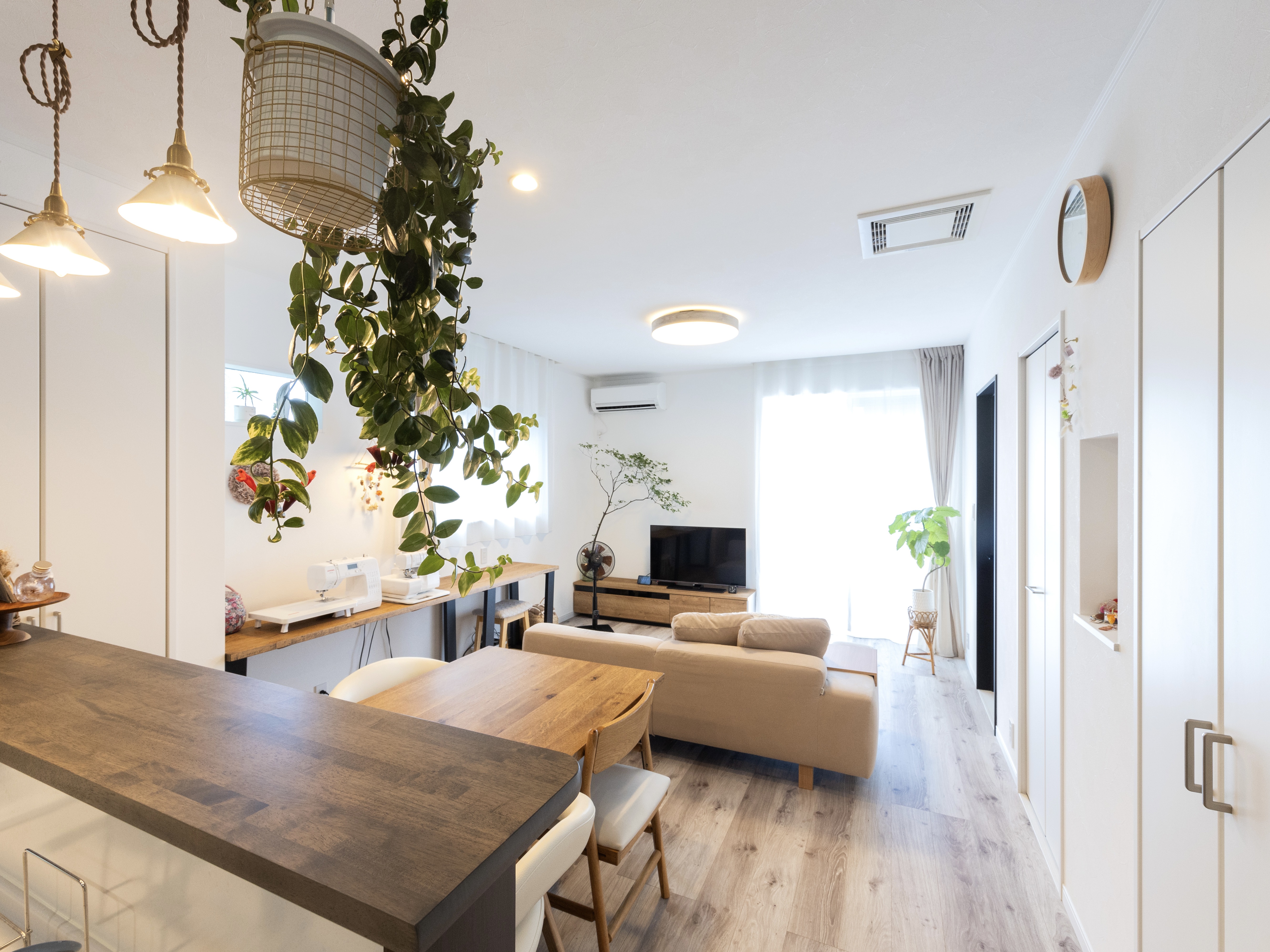 エスホーム｜明るく開放的なリビングダイニング。シックな木材のダイニングテーブルと、壁に設置された緑が温かみを与えている。