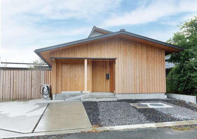 平屋のようにも見える落ち着いた雰囲気の外観デザイン。薄いグレーの左官壁とガルバリウムの壁、玄関周りは押縁の杉板張りで仕上げた。将来の暮らしに備えてV2Hも導入済み。屋根そのものが太陽光パネルになった「エコテクノルーフ」を採用し、漏水もなく工事もメンテナンスも楽々