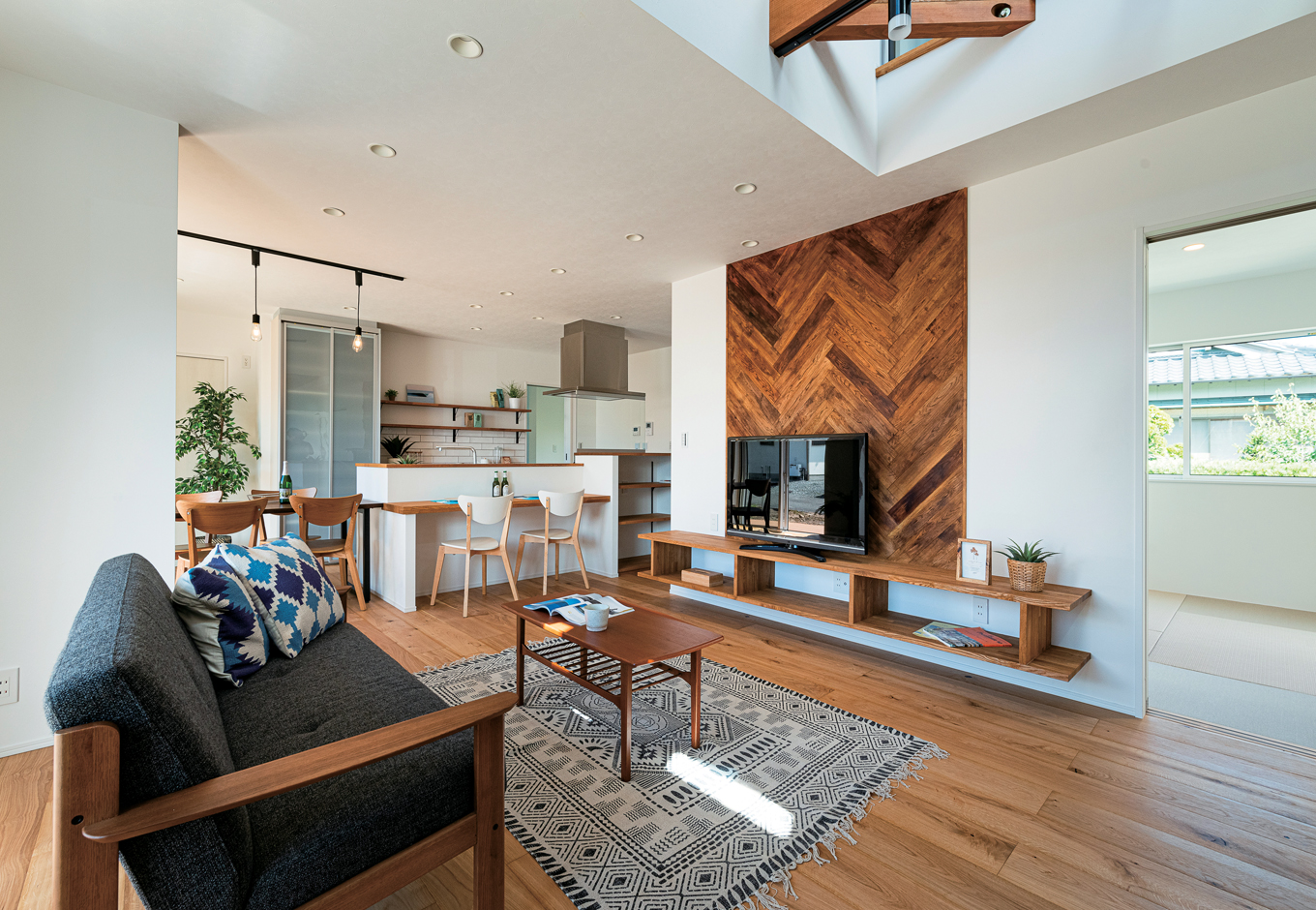 KUREKEN HAUS（榑林建設）【デザイン住宅、省エネ、間取り】吹き抜けのあるLDKを中心に和室、ウッドデッキ、2階までつながる圧倒的な開放感。LDKには無垢の床板を採用。
テレビ背景の壁には、西海岸スタイルを感じられるヘリンボーンの板張りでアクセントを。